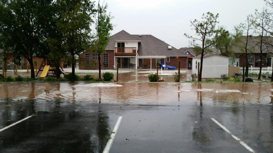 Flood waters between a large home and a parking lot for a business