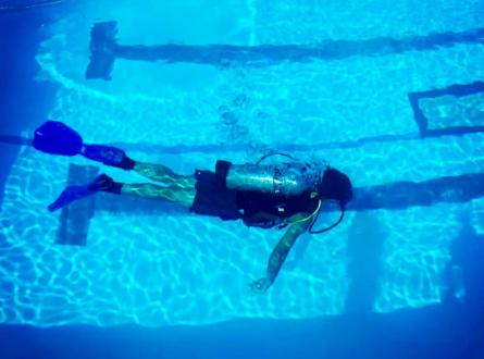 A scuba diver swims underwater in the dive well. 