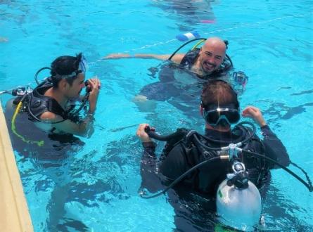 Scuba divers listen to instructor above the water. 